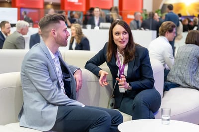 Ein junger Mann und eine junge Frau unterhalten sich sitzend auf einem Messestand.